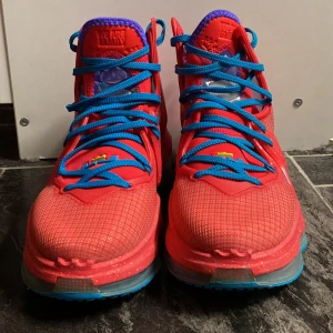 Nike LeBron röd/blå sneakers - Färgstarka Nike LeBron sneakers i rött med blå snören och detaljer, lila insida och transparent sula. Snygg mesh- och syntetmix, högt skaft och coola grafiska detaljer på plösen och hälen. Perfekta för dig som vill sticka ut med din stil.Tyvärr så tillkommer inte boxen. Skorna kommer tyvärr i en annan box. Varan är använd 1-2 gånger och är storlek 40.