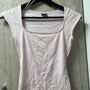 Ljusrosa ärmlös topp med fyrkantig ringning - Supersöt ljusrosa topp från Bershka med en snygg fyrkantig ringning och ärmlös design. Tunn och mjuk bomullskvalitet som känns skön mot huden. Perfekt att styla med jeans eller kjol för en chill look. Ny aldrig använd