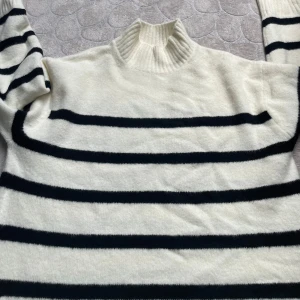 Randig polotröja från GU, vit och svart - Säljer en mysig vit polotröja från GU med svarta horisontella ränder. Tröjan har ribbad hög krage och långa ärmar. Perfekt för lager-på-lager och chill höst- eller vinterstil. Materialet är mjukt och stickat för extra komfort. Den är köpt i Japan och är väldigt fin