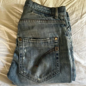 Dondup George jeans - Säljer ett par ljusblå jeans från dondup med snygga slitningar och trasiga detaljer på benen. Jeansen har klassisk femficksdesign, normal passform och raka ben. Perfekta för dig som gillar en avslappnad och trendig look.