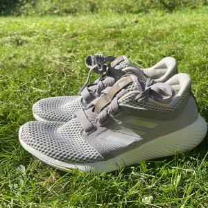 Adidas Edge Lux grå sneakers - Snygga Adidas Edge Lux sneakers i ljusgrått meshmaterial med vita detaljer och klassiska tre ränder på sidan. Skorna har snörning, platt sula och ventilerande ovandel som passar perfekt för träning eller en aktiv vardag.