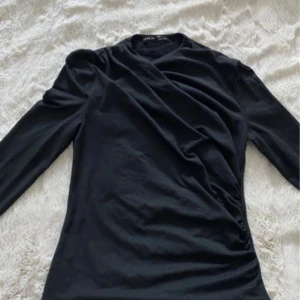 Svart omlottop från SHEIN - Snygg svart omlottop från SHEIN med lång ärm och draperad effekt framtill. Toppen har en figurnära passform och är perfekt för dig som gillar stilrena plagg med en twist. Tillverkad i mjukt material som känns skönt mot huden.