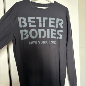 Svart långärmad tröja Better Bodies - Svart långärmad tröja från Better Bodies med stort tryck i grått framtill där det står 'BETTER BODIES NEW YORK 1982'. Tröjan har rund halsringning och är tillverkad i mjuk bomull, perfekt för träning eller chill.