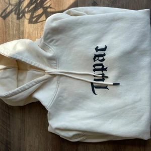 Vit 2Pac hoodie från Pull&Bear - Säljer en vit hoodie från Pull&Bear med stor svart 2Pac-print på framsidan och coolt tryck med Tupac Shakur. Tröjan har huva med snörning och är i mjuk bomull. Perfekt för dig som gillar streetwear och vill sticka ut med en ikonisk look.