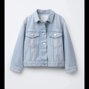 Ljusblå jeansjacka från Zara - Snygg ljusblå jeansjacka från Zara med klassisk krage, silverfärgade knappar och två bröstfickor med lock. Jackan har raka ärmar och en avslappnad passform, perfekt att slänga över en hoodie eller t-shirt. Enkel och stilren design som funkar till allt.
