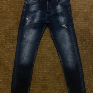Mörkblå slim jeans från Dsquared2 - Snygga mörkblå slim jeans från Dsquared2 med slitningar och färgstänk på framsidan. Jeansen har klassisk femficksdesign, låg midja och tydliga tvättade detaljer för en cool, använd look. Perfekta för dig som gillar streetstyle och vill sticka ut.