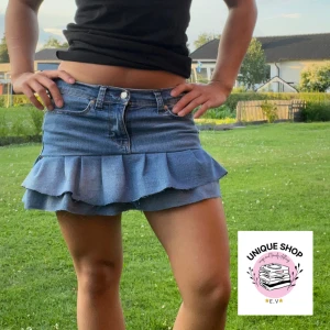 Jeanskjol med volang från U.S. Polo Assn. - Superfin blå jeanskjol från U.S. Polo Assn. med volangkant nertill. Klassisk femficksmodell, bälteshällor och broderad logga i midjan. Kjolen är kort och har en snygg, avslappnad vibe som passar perfekt till sneakers eller boots. Midje: 36-37cm och längd: 35cm 