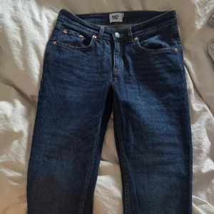 Mörkblå straight/bootcut jeans från 157 - Snygga mörkblå jeans från 157 med klassisk femficksdesign och bootcut-ben. De är i straight modellen men såg bootcut ut på mig. Jeansen har hög midja och är tillverkade i mjukt denimtyg med stretch för extra komfort. Bakfickorna har lock med knappdetalj som ger en cool touch.