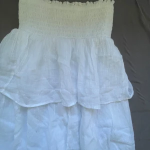 Vit sommarklänning från Gina Tricot - Supersöt vit klänning från Gina Tricot med smock upptill och volangig kjol. Axelbandslös modell i luftig bomull, perfekt för varma dagar. Enkel och fräsch stil som passar till många tillfällen. Använd 1 gång 💕