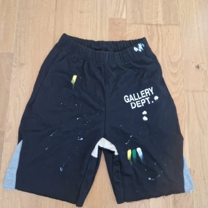  Gallery Dept. shorts - Svarta shorts från Gallery Dept. i 100% bomull med elastisk midja och råa benslut. Unik design med färgstänk i vitt, gult och grönt samt tryckt logga på framsidan. Gråa paneler på sidorna ger en cool kontrast. Perfekta för dig som gillar streetwear med edge. Helt nya!!!