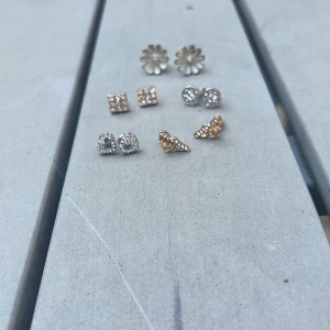 Set med sex par glittriga örhängen - Säljer ett set med sex par örhängen i olika former: blommor, hjärtan, fjärilar, runda och fyrkantiga studs. Färgerna är guld och silver, alla med glittrande stenar. Perfekt för att mixa och matcha till olika looks.