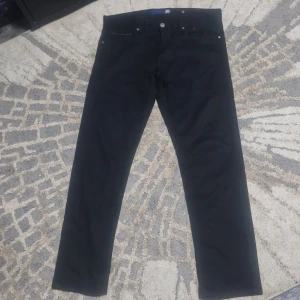 Jeans Replay RBJ - Svarta straight jeans från Replay RBJ med klassisk femficksdesign och raka ben. Jeansen har metallknappar och nitar, samt diskret logga på bakfickan. Snygg och stilren modell i svart denim som passar till allt. 