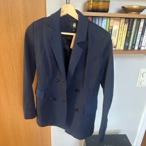 Mörkblå kavaj från G-Star RAW, S - Snygg mörkblå kavaj från G-Star RAW i klassisk dubbelknäppt modell. Kavajen har två fickor framtill, smala slag och knappar vid ärmslut. Perfekt för en stilren look och passar till många olika outfits.