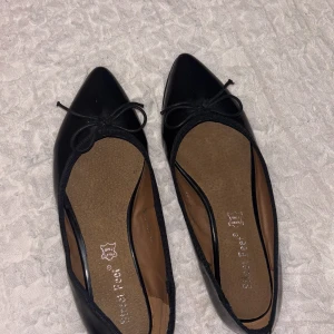Svarta ballerinaskor med rosett - Snygga svarta ballerinaskor från Street Feet med spetsig tå och liten rosett framtill. Skorna är i skinn med mjuk innersula och har en klassisk, stilren look. Perfekta för dig som gillar enkel men elegant stil.