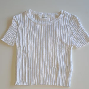 Vit ribbad topp från H&M - Säljer en fräsch vit ribbad topp från H&M. Tyget är stretchigt och kan även passa en XS. Perfekt att matcha med jeans eller kjol för en clean look. 💕