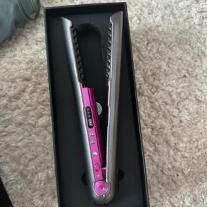 Trådlös plattång i silver och rosa - Säljer en trådlös plattång i metallic silver och rosa med digital display och flera värmeinställningar. Kommer i originalförpackning med laddstation, USB-kabel och svart förvaringspåse. Perfekt för att styla håret snabbt och smidigt utan sladd.