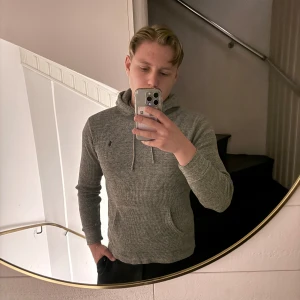 Grå hoodie från Polo Ralph Lauren - Säljer en gråmelerad hoodie från Polo Ralph Lauren med diskret logga på bröstet. Tröjan har huva med snörning, känguruficka och är tillverkad i mjukt stickat material. Perfekt för chill dagar eller när du vill vara extra bekväm. Sitter mer som S