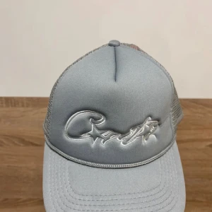 Ljusgrå Corteiz Keps - Snygg ljusgrå keps med silvrigt broderat logotyp och stjärndetalj framtill. Kepsen har klassisk böjd skärm och mesh på sidorna och bak för extra ventilation. 
