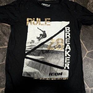 Svart t-shirt med guldtryck Firefly stl 146-152 - Cool svart t-shirt från Firefly med stort tryck i vitt, svart och guld. Framsidan har texten 'Rule Breaker', en skateboard-illustration och siffran 28 i metallicguld. Skön passform och perfekt för streetwear-stil.