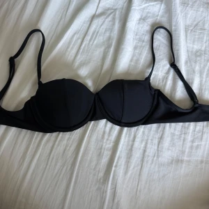 Svart bikiniöverdel med bygel - Stilren svart bikiniöverdel med bygel och vadderade kupor. Justerbara axelband och klassisk knäppning bak. Snygg och enkel modell som passar till det mesta på stranden eller vid poolen. Storlek XS och använd 1-2 gånger.💕den vita lappen är klippt då den stördes vid användning.