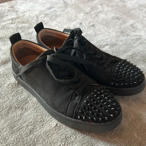 Svarta Louboutin sneakers med nitar - Snygga svarta sneakers från Christian Louboutin med mattsvarta nitar på tån och klassisk röd sula. Det har stått Louboutin på insidan med det har suddats ut lite så man bara ser L