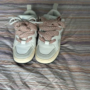 Vita sneakers med mönstrade snören -  Steve Madden skor med rosa och vita snören i fiskbensmönster. Skorna har en beige sula, svarta detaljer undertill och en mix av skinn och mocka på ovandelen. Skorna är använda två gånger då jag själv inte tycker jag passar i dom. Dom är små i storleken har i vanliga fall storlek 37 och det är 38 i dessa