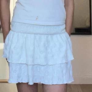 Vit volangkjol från Gina Tricot - Supersöt vit kortkjol från Gina Tricot med broderade blommor och volanger. Kjolen har resår i midjan men dem tre högst uppe är borta och är gjord i ett lätt bomullstyg, perfekt för varma dagar. Den har en romantisk och luftig känsla med fina detaljer. Pris går att diskuteras 