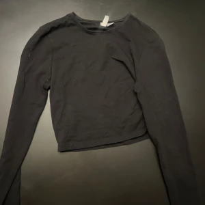 Svart croppad långärmad tröja - En enkel svart croppad långärmad tröja i mjuk bomull. Perfekt till jeans eller kjol för en clean och stilren look. Tröjan har rund halsringning och sitter snyggt med sin normala passform.