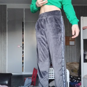 Grå mjukisbyxor Cool Club Moonlight - Mörkgrå mjukisbyxor från Cool Club med texten 'MOONLIGHT' längs båda sidorna. Byxorna har resår i midjan och vid bensluten för en skön passform. Tillverkade i mjukt, sammetsliknande material som känns riktigt bekvämt.