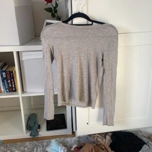 Beige långärmad tröja i bomull - En enkel genomskinlig och stilren beige långärmad tröja i mjuk bomull. Tröjan har en rak passform och rund halsringning, perfekt att matcha med jeans eller kjol för en clean look.
