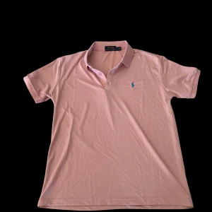 Rosa pikétröja från Polo Ralph Lauren - Snygg rosa pikétröja från Polo Ralph Lauren med klassisk krage och korta ärmar. Tröjan har blå broderad logga på bröstet och är gjord i bomull för en skön och luftig känsla. Perfekt för en clean och stilren look. Priset går att diskuteras // VTCLOSET 