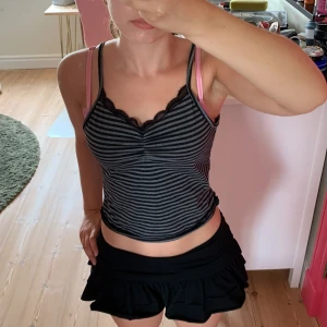 Randig svart-grå linnetopp med spets - Säljer en croppad linnetopp med tunna axelband i svart och grått randigt mönster. Toppen har söt spetskant vid urringningen och en liten rynkdetalj framtill. Perfekt för dig som gillar en enkel men ändå snygg stil.