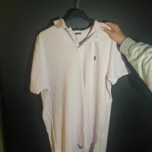 Ljusrosa pikétröja från Ralph Lauren - Säljer en ljusrosa pikétröja från Polo Ralph Lauren i modellen Custom Slim Fit. Tröjan har klassisk krage, korta ärmar och knäppning med två knappar. Ikoniska blå loggan broderad på bröstet. Perfekt för en clean och stilren look. Priset är inte hugget i sten utan kan lätt diskuteras vid enkel affär!