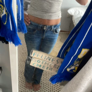 Blå bootcut jeans från Gina Tricot - Säljer ett par blå bootcut jeans från Gina Tricot med låg midja/mid waist och snygga slitningar framtill. Jeansen har dubbla knappar i midjan, klassiska fickor och kontrastsömmar. Perfekta för dig som gillar 00-talsvibbar och vill ha en avslappnad men trendig look.