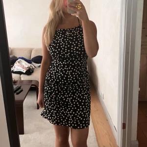 Svart prickig kort klänning med smala band - Supersöt svart kort klänning från H&M med vita prickar och smala axelband som korsas i ryggen. Figurnära passform och rak halsringning, perfekt för dig som gillar en lekfull och trendig stil. Oanvänd ❤️