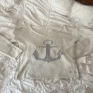 Beige stickad tröja med ankare från bondelid - Säljer en beige stickad tröja från bondelid med ett stort grått ankare framtill. Tröjan har lång ärm,  v halsringning och är perfekt för dig som gillar en chill och nautisk vibe. Broderad bondelid logga nertill. Supermjuk och skön att ha på sig!