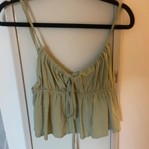 Ljusgrön linnetopp med knyt - Supersöt ljusgrön linnetopp med smala axelband och knyt framtill. Toppen har en luftig och flowy passform med rynkade detaljer och v-ringning. Perfekt för varma dagar och enkel att styla till jeans eller kjol.