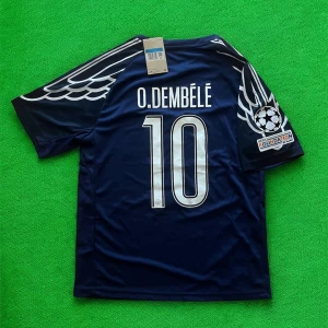 PSG Dembélé #10 fotbollströja blå - Snygg PSG fotbollströja i mörkblått med O. Dembélé och nummer 10 på ryggen. Tröjan har vita detaljer, vingmönster på axlarna, Champions League-märke på ärmen och Qatar Airways-logga framtill. Tillverkad i lätt och ventilerande material.