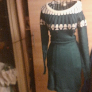 Grön stickad klänning från Ellos - Mysig grön stickad klänning från Ellos med vit mönstrad krage och långa ärmar. Klänningen har en figurnära passform och ett snyggt mönster upptill som ger retrovibbar. Perfekt för dig som gillar stickade plagg med lite extra detaljer.