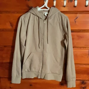 Beige hoodie från H&M med dragkedja - En beige hoodie från H&M i storlek S. Tröjan har dragkedja framtill, huva med snörning och två fickor. Perfekt för chill dagar och enkel att matcha med jeans eller mjukisbyxor. Tillverkad i mjuk bomullsmix för skön känsla.