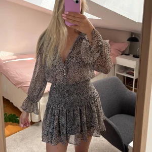 Leopardmönstrad kortklänning från Zara - Supersöt kortklänning från Zara med leopardmönster i beige och bruna toner. Klänningen har långa ärmar med volang vid ärmslut, v-ringning med knappar och smockad midja som ger en snygg passform. Tunt, lätt material som känns luftigt och fint. Väldigt bra skick o nästan aldrig använd