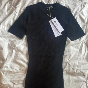Svart ribbad stickad klänning från Gina Tricot - Kortärmad svart stickad klänning från Gina Tricot i storlek S. Klänningen har ribbad struktur, rund halsringning och en tight passform som framhäver figuren. Perfekt för en stilren och enkel look.