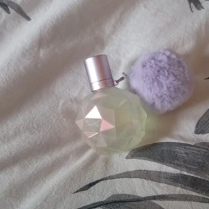 Ariana Grande parfym med lila fluffboll - Säljer en Ariana Grande parfym i en diamantformad, transparent flaska med pastellskiftningar och ett ljust lila lock. Flaskan har en stor, mjuk lila fluffboll som dekoration. Perfekt för dig som gillar söta och fruktiga dofter. Lilla fliffbollen ramlade av för länge sen och då så lagade jag den det är mer synlig på bild 3 😁 