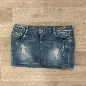 Blå jeanskjol från J-welly - Säljer en blå jeanskjol från J-welly med slitna detaljer och klassiska fickor både fram och bak. Kjolen har knapp- och dragkedjestängning samt bälteshällor. Perfekt för dig som gillar en avslappnad och trendig stil.