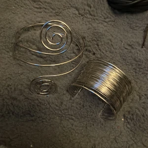 Silvriga armband i metalltråd - Två unika armband i silverfärgad metalltråd. Ett armband har en spiralformad design och det andra är bredare med flera varv av tunn tråd som ger en cool, modern look. Perfekta för att ge din outfit en edgy touch.