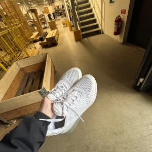 Vita 270 Nike skor - Säljer ett par fräscha vita air 270 sneakers från Nike med stickad ovandel och snörning. Skorna har en sportig design med rund tå och platt sula, samt detaljer i syntetmaterial. Perfekta för dig som gillar stilrena och bekväma skor.