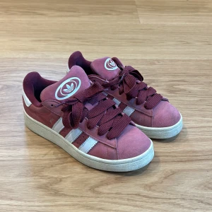 Adidas Campus sneakers rosa och vinröd mocka - Säljer ett par Adidas Campus sneakers i rosa mocka med vita ränder och logga på plösen. Skorna har breda vinröda skosnören och vit sula. 