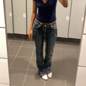 Miss me blåa jeans från LA Idol USA - Säljer ett par blå jeans från LA Idol USA med snygga broderade detaljer och pärlor på bakfickorna. Jeansen har vita kontrastsömmar och låg midja. Passformen är bootcut och materialet är klassisk denim.