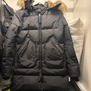 Svart dunjacka med fuskpäls från Parajumpers - Säljer en svart lång dunjacka från Parajumpers med huva och päls.Jackan har dragkedja framtill, stora fickor med lock och ribbade muddar vid ärmslut. Perfekt för kalla dagar och riktigt snygg passform. Priset går att disponeras