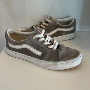 Gråa Vans skor - Säljer ett par klassiska Vans skor sneakers i grå mocka med vit sula och vit sidoremsa. Skorna har snörning och den ikoniska Vans-loggan baktill. Perfekta för en avslappnad streetstil. Det är i ganska bra skick och är i storlek 39.
